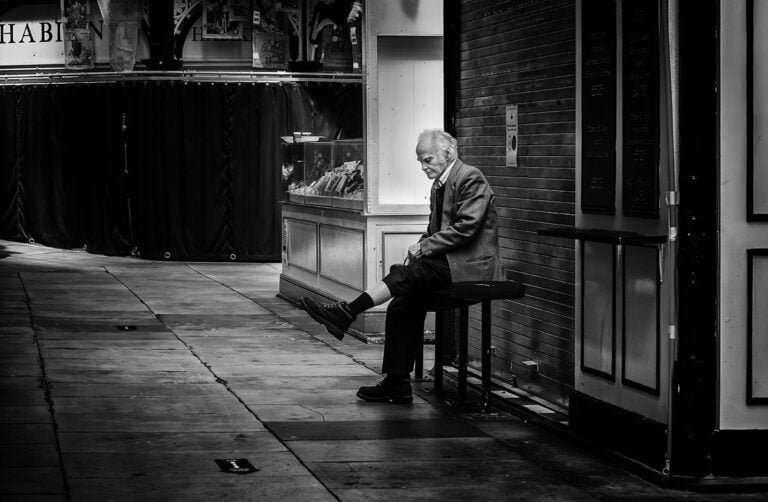 A man sitting on a bench in front of a building.