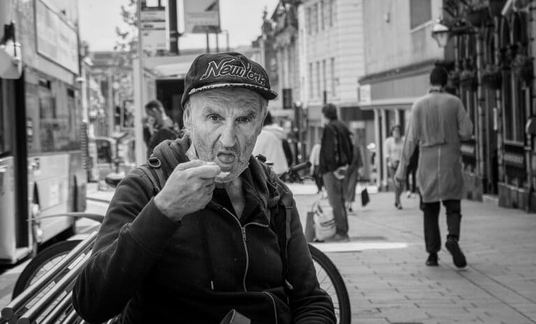 A black and white photo of an old man sitting on a bench.