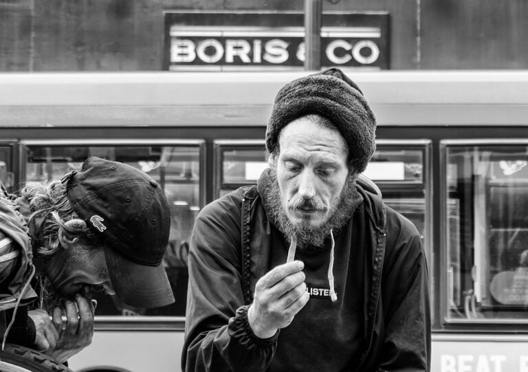 Black and white photo of a homeless man in front of a bus.
