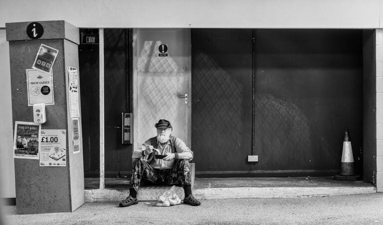 A man sitting on a bench in front of a building.