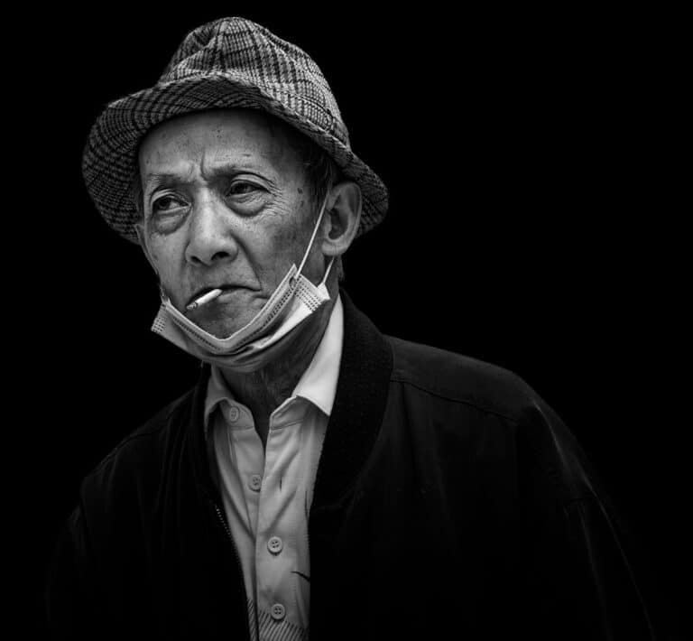 A black and white photo of an old man smoking a cigarette.