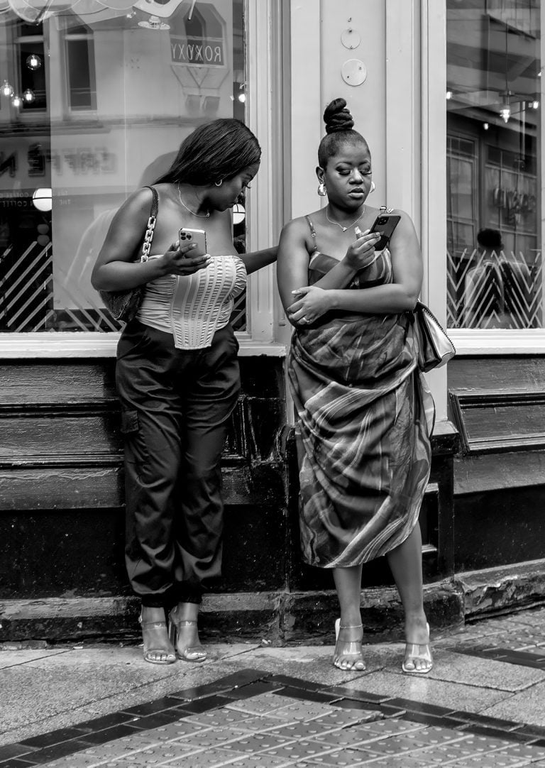 20230708-IMG_6996-Edit Two women standing in front of a store looking at their phones.