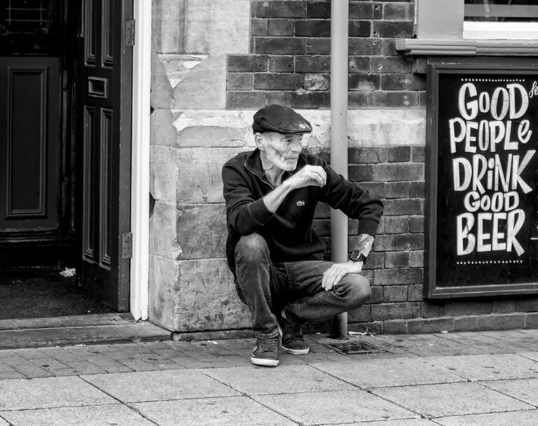 A man kneeling in front of a sign that says good people drink beer.