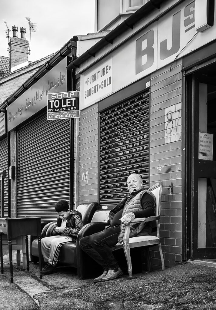 A man is sitting on a couch in front of a store. A man is sitting on a couch in front of a store.