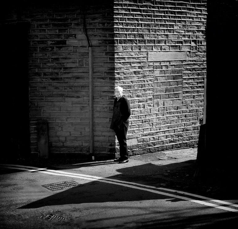 A black and white photograph of a man standing on a street.
