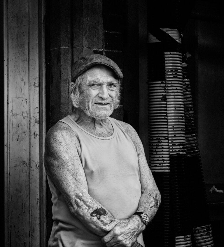 An old man with tattoos standing in front of a door.