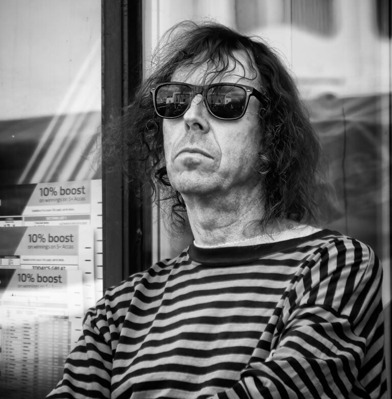 A man in a striped shirt is sitting in front of a window.