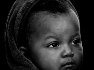 A black and white photo of a baby wearing a hood.