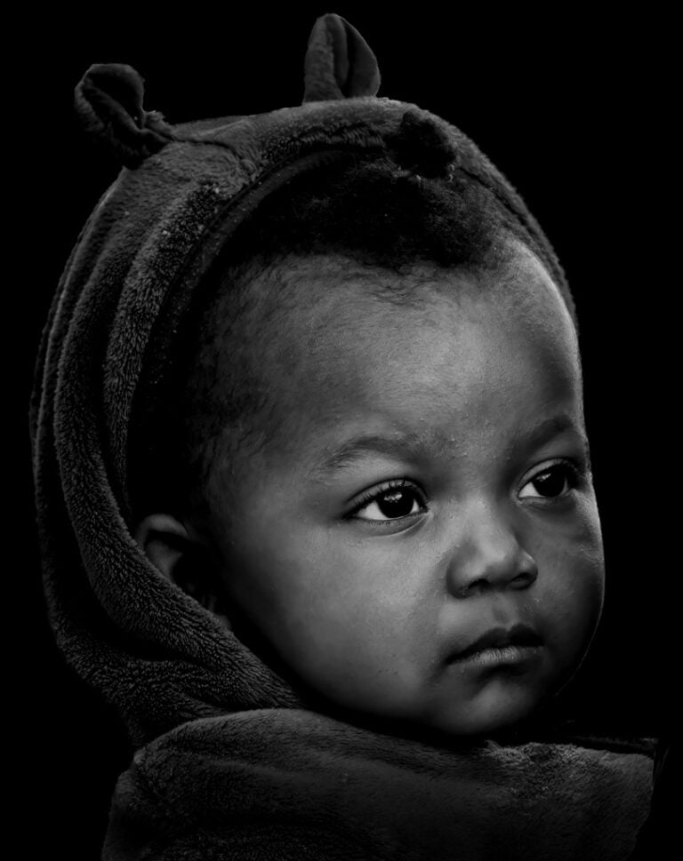 A black and white photo of a baby wearing a hood. A black and white photo of a baby wearing a hood.