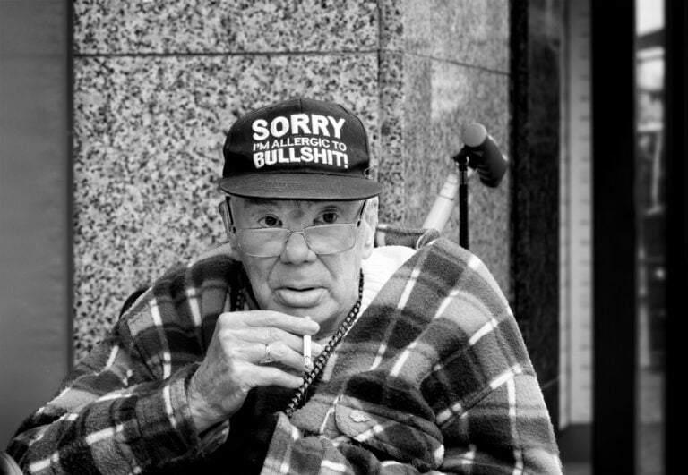 A black and white photo of an old man smoking a cigarette.