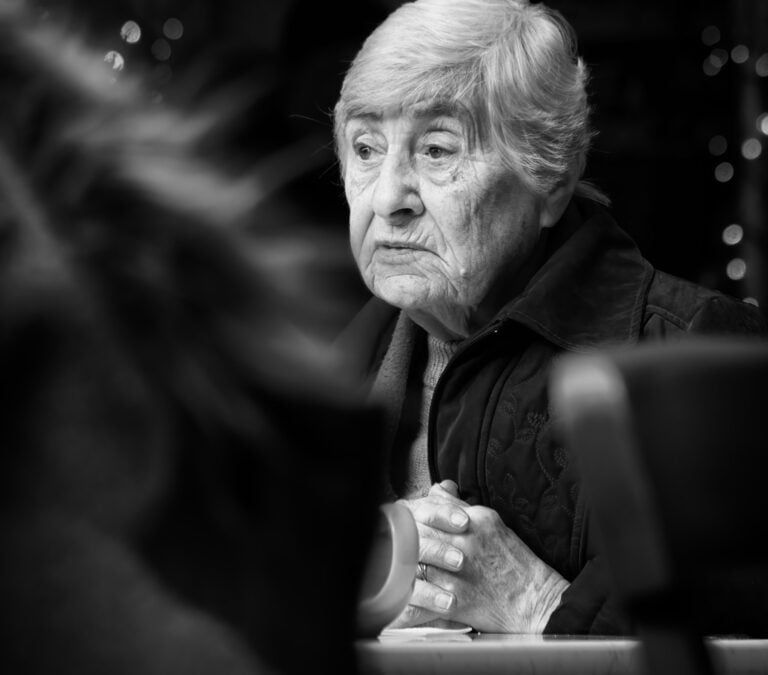 An older woman sitting at a table with a cup of coffee.