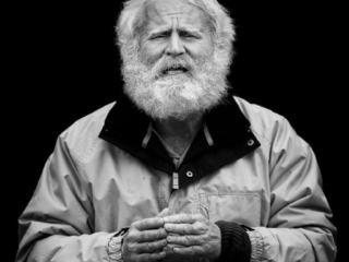 An old man with a beard sitting on a chair.
