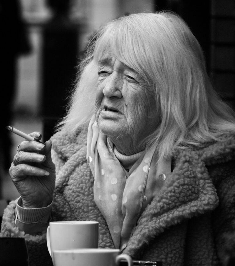 An old lady smoking a cigarette at a cafe.