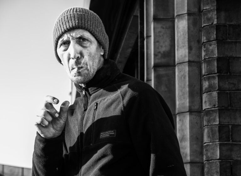 A man smoking a cigarette in front of a building.