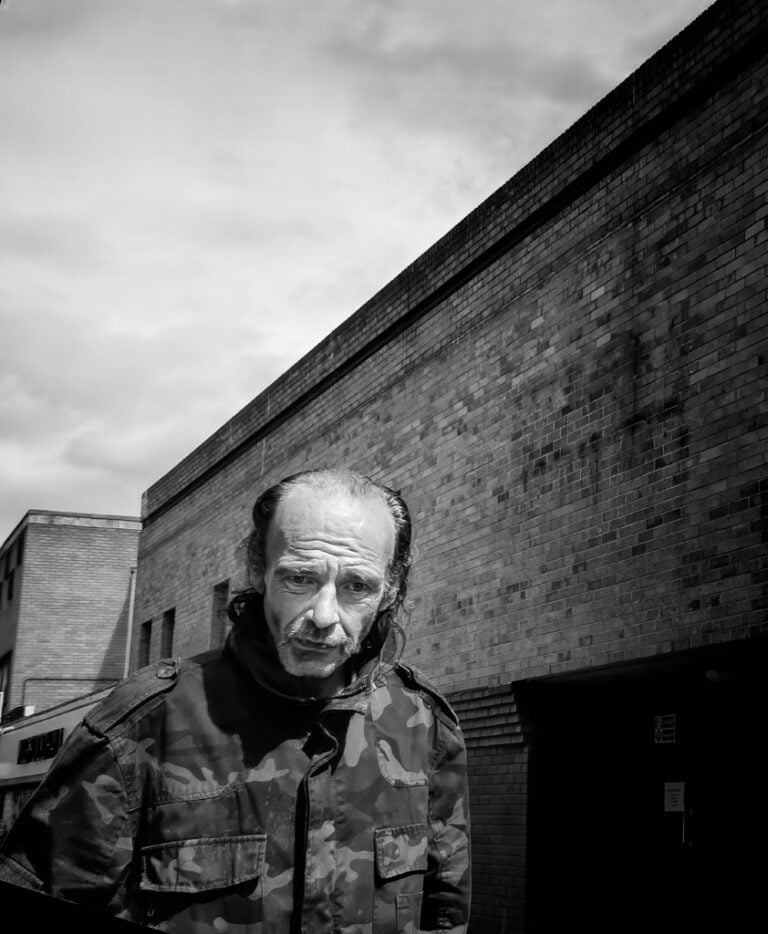 A man in a camouflage jacket standing in front of a building.