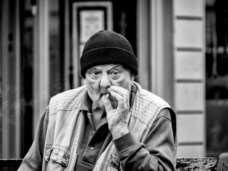 An old man smoking a cigarette on a bench.