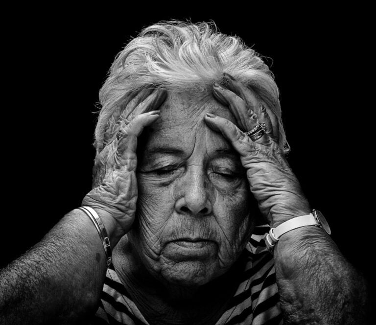 A black and white photo of an old woman with her hands on her head. A black and white photo of an old woman with her hands on her head.