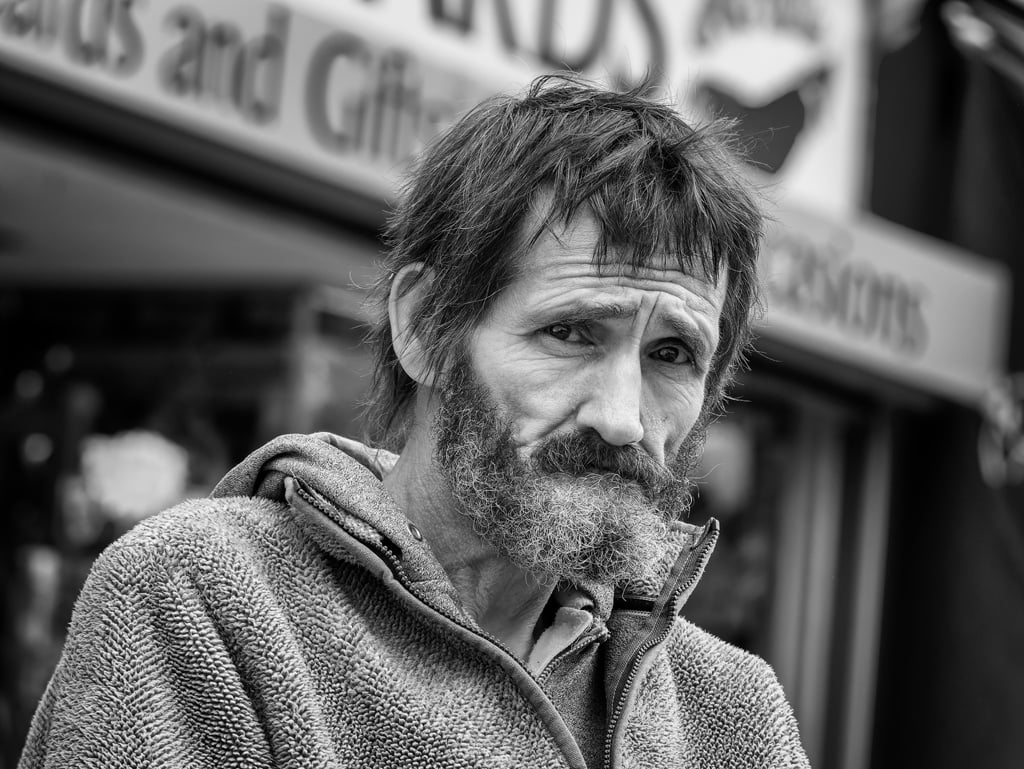 A homeless man standing in front of a store.