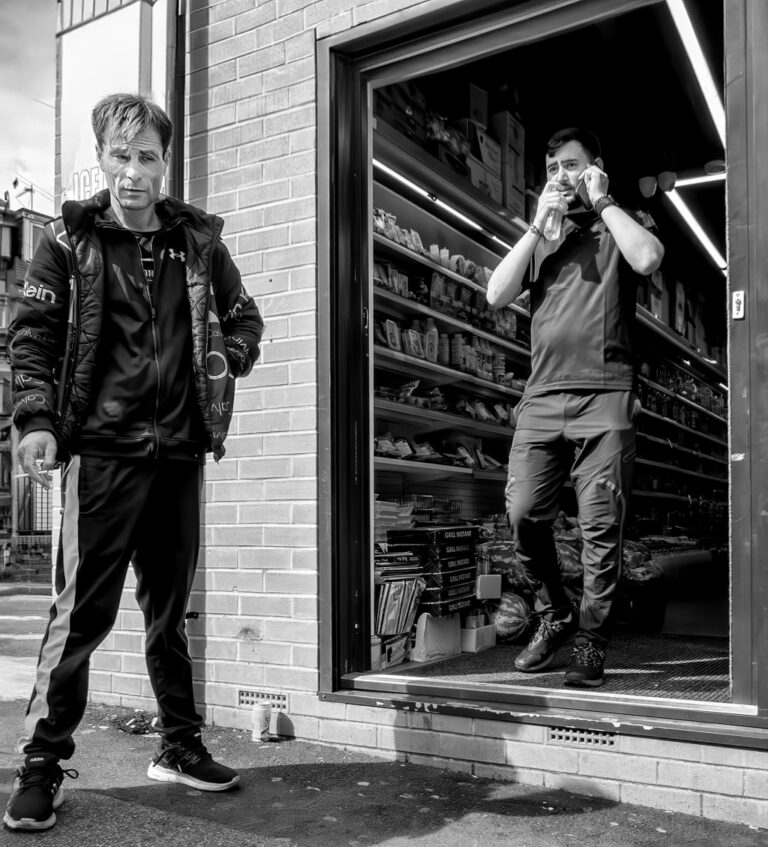 AUGUST Two men standing in front of a store.