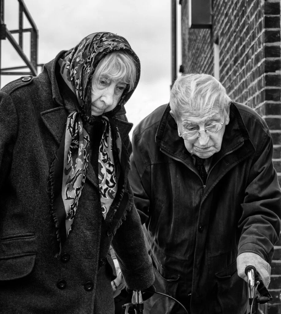 A black and white photograph of an elderly couple walking down the street.