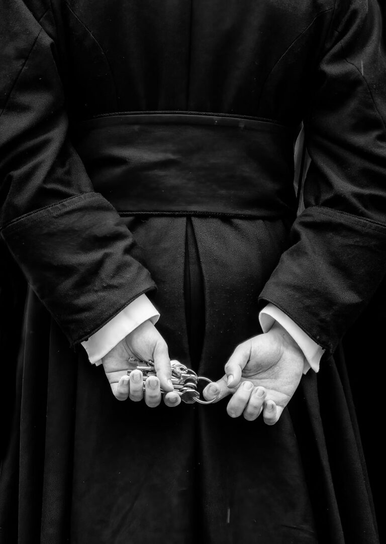 JUNE A black and white photo of a priest in a robe holding some keys.