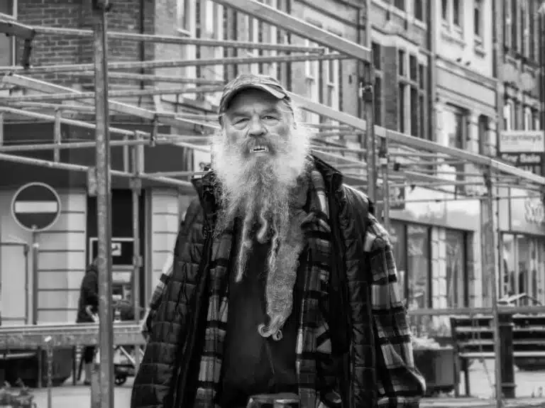 A man with a long beard standing on the street.