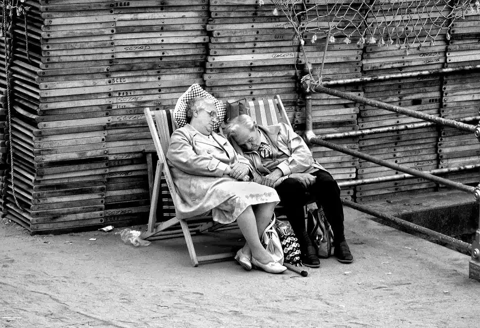 A black and white photo of two people sleeping on a deck chair.