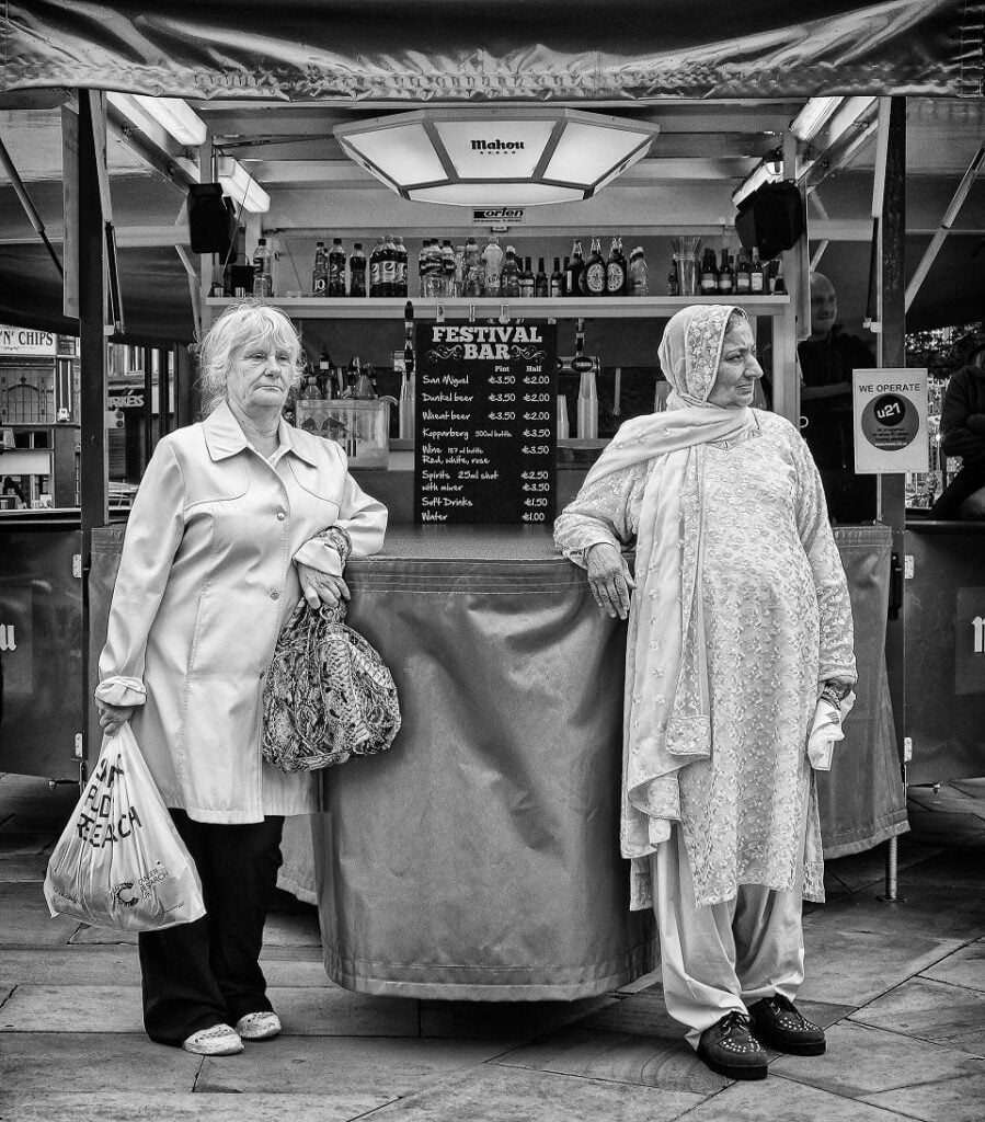 Two women standing in front of a food cart.