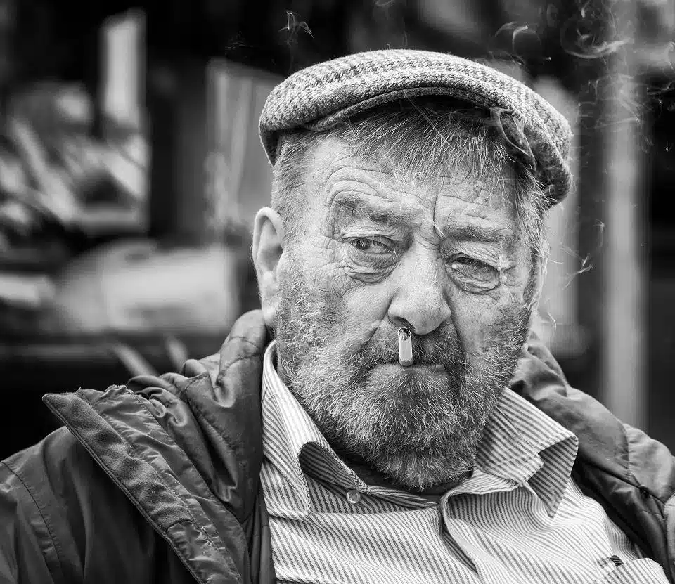 A black and white photo of an old man smoking a cigarette.