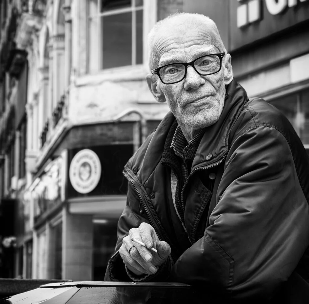 A man with glasses leaning against a wall.