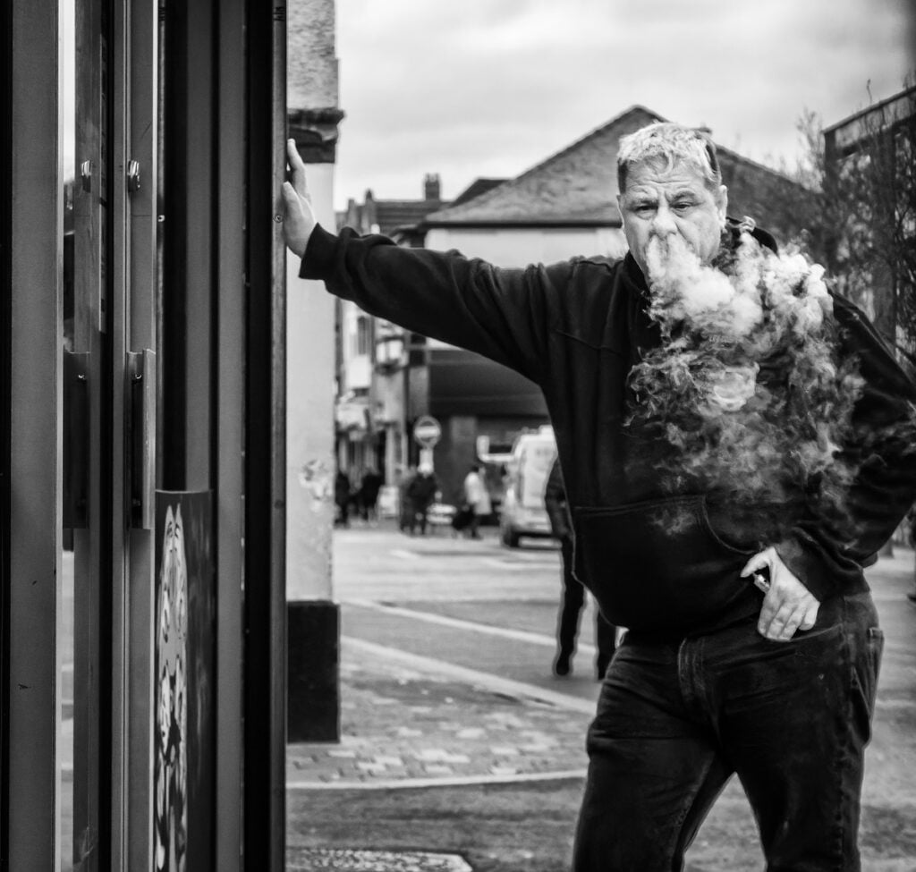 A man smoking a cigarette in front of a shop.