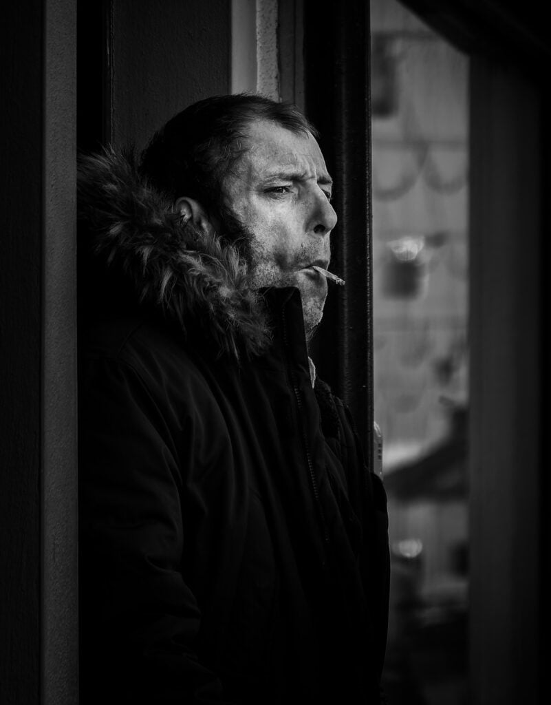 A man smoking a cigarette out of a window.
