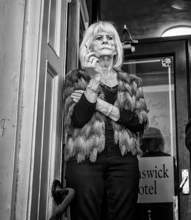 A woman is standing in front of a door with a cigarette in her hand.