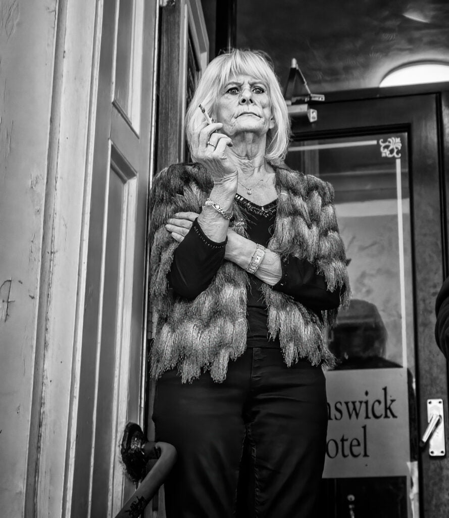 A woman is standing in front of a door with a cigarette in her hand.