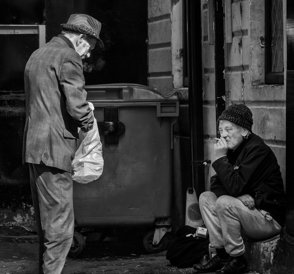Black and white photograph of a man and woman sitting on the street.
