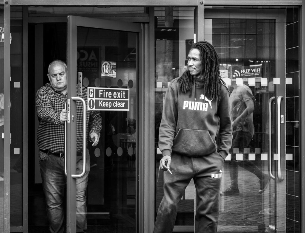 Two men standing in front of a glass door.