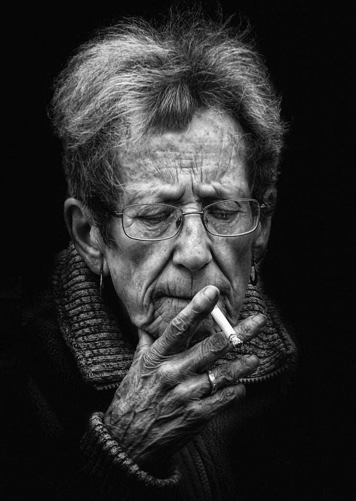 A black and white photo of an old woman smoking a cigarette.