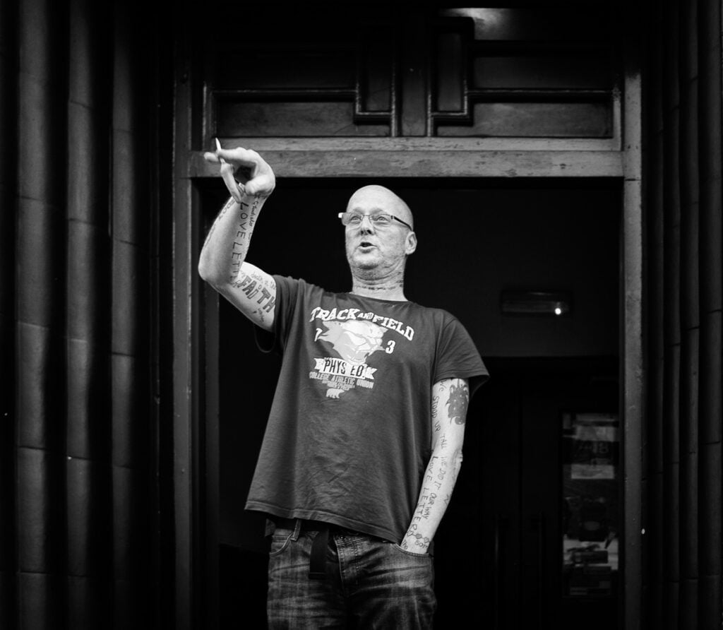 A black and white photo of a man standing in front of a door.
