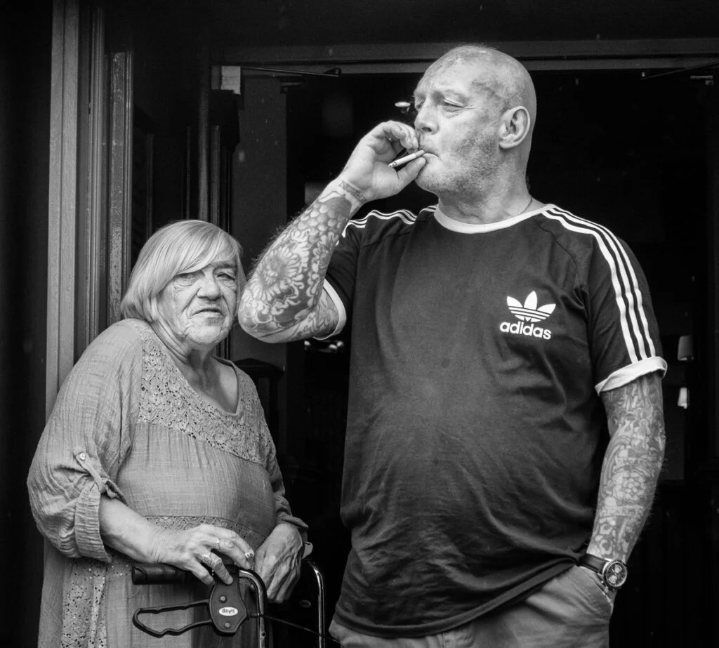 A man and woman smoking a cigarette in front of a door.