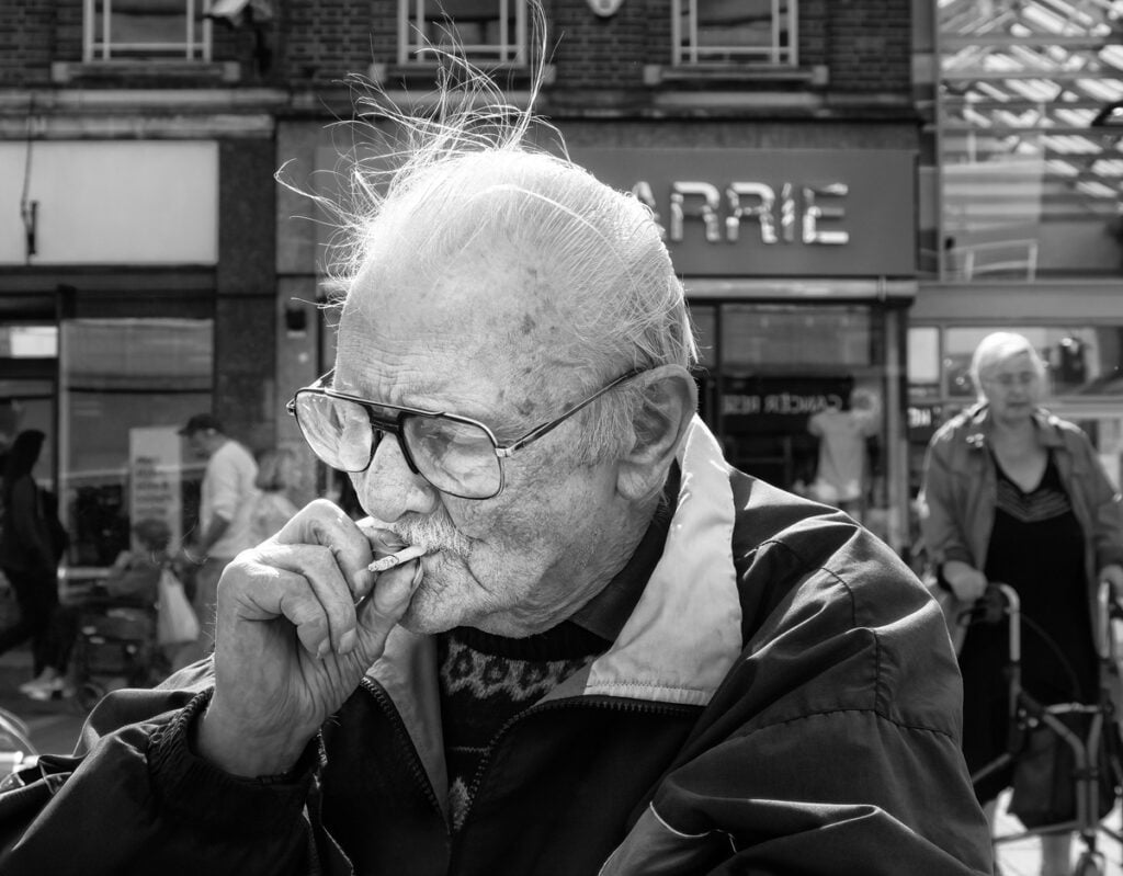 Black and white photograph of an old man smoking a cigarette.