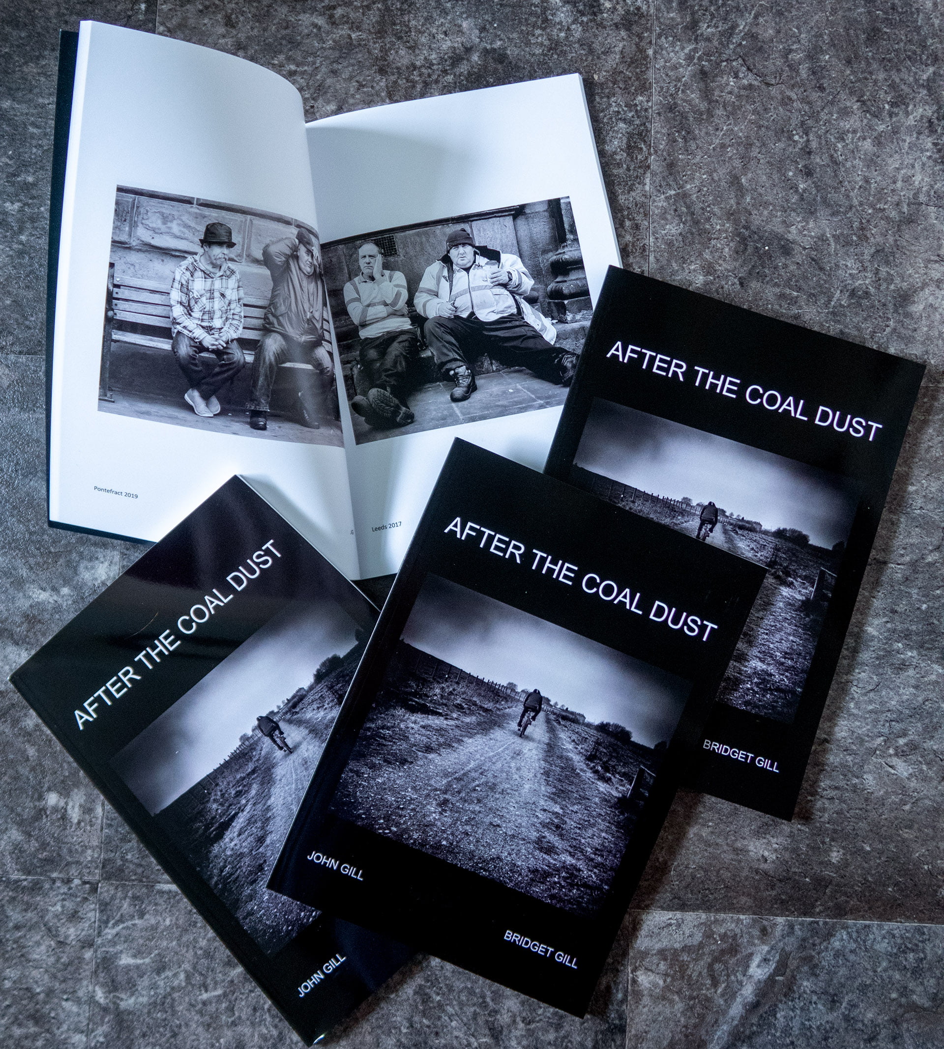 After the Coal Dust book - Softcover version 10 Two open photo books titled "after the coal dust" by bridget and john gill laid on a tiled floor, displaying black and white images of individuals and landscapes.
