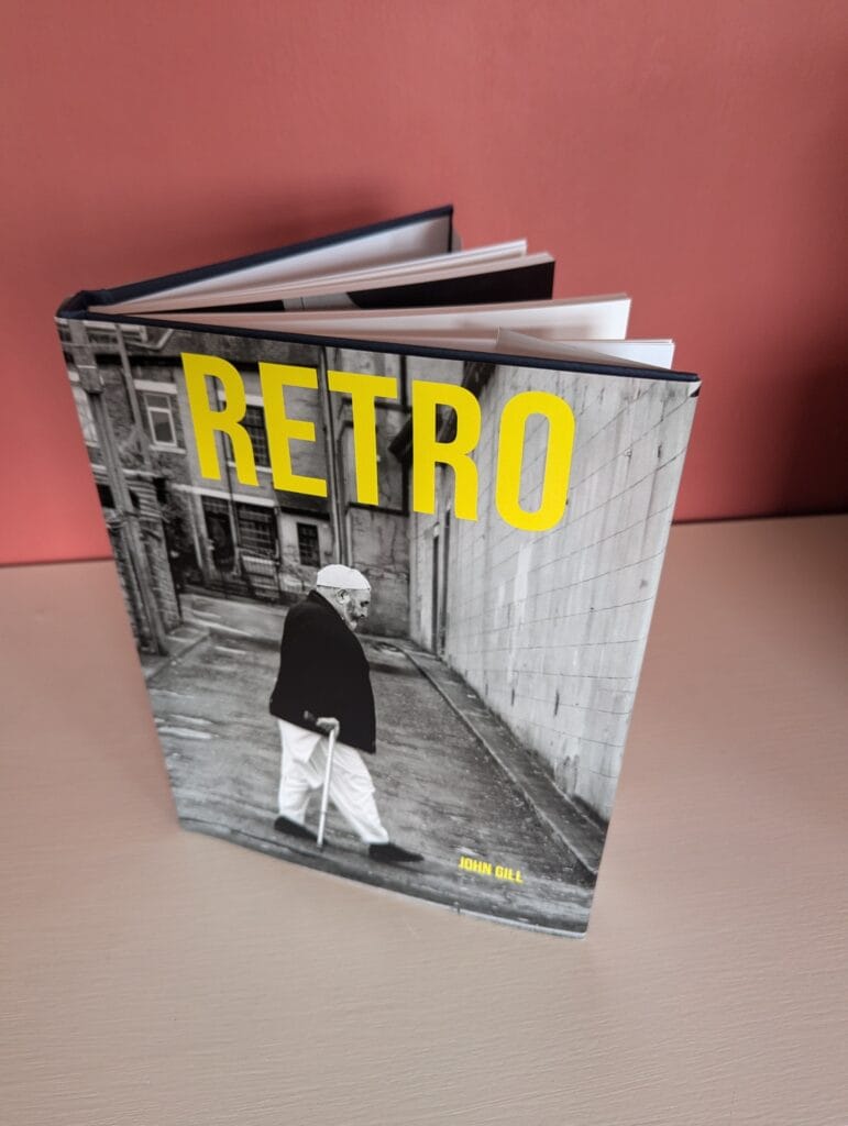 Cover of a book titled "Retro" by John Dell, featuring a grayscale image of an elderly person with a walking stick against an urban background.