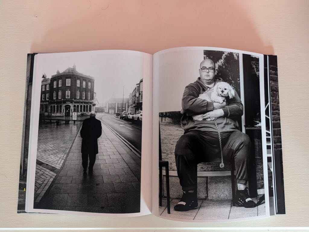 Open photo book showing two black and white images: a person walking on a street, and a person seated with a small dog.