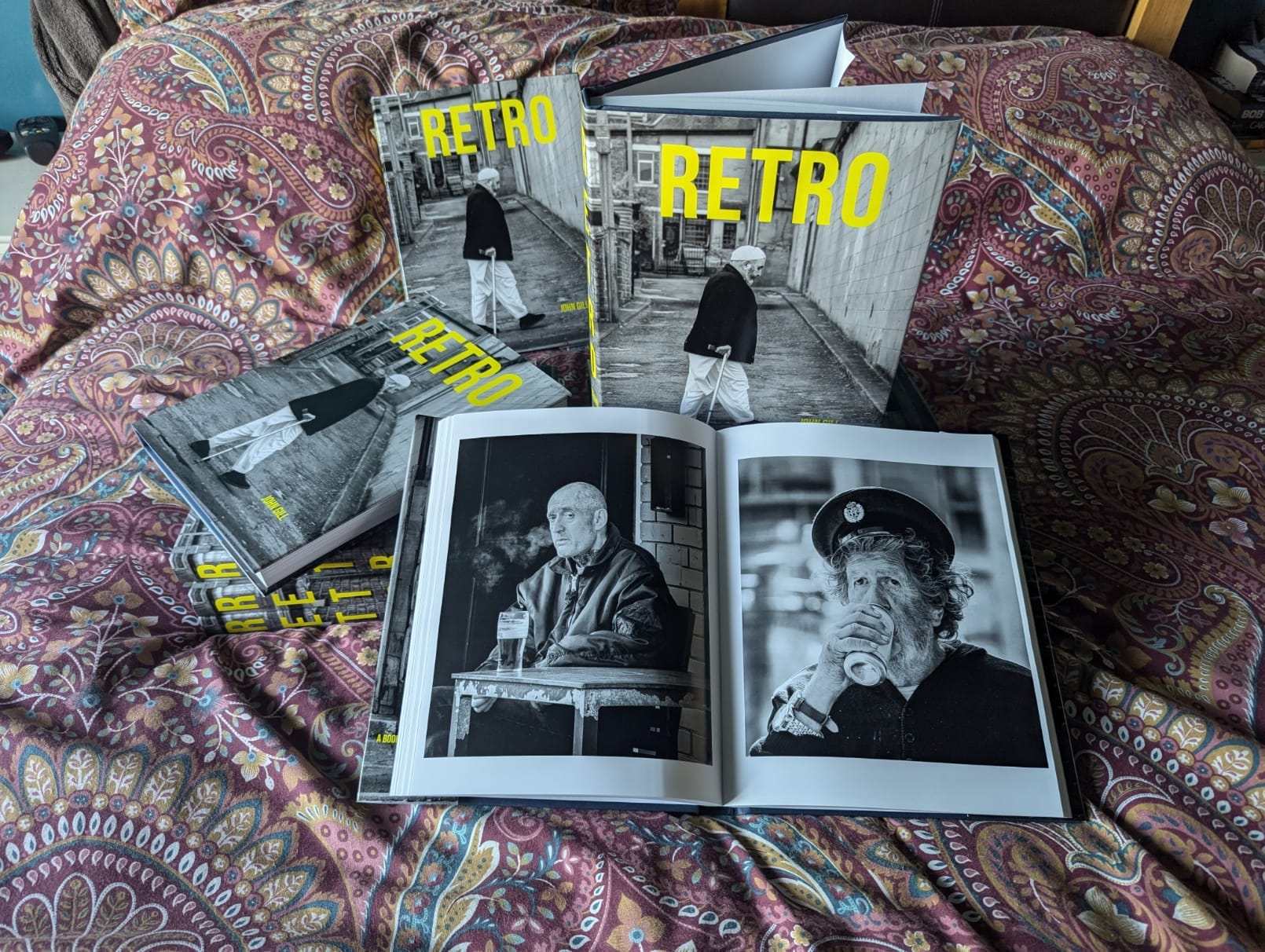 RETRO - a 300 page retrospective. 8 Books titled "Retro" are displayed on a patterned bedspread, with one open showing black and white photos of a man at a table.