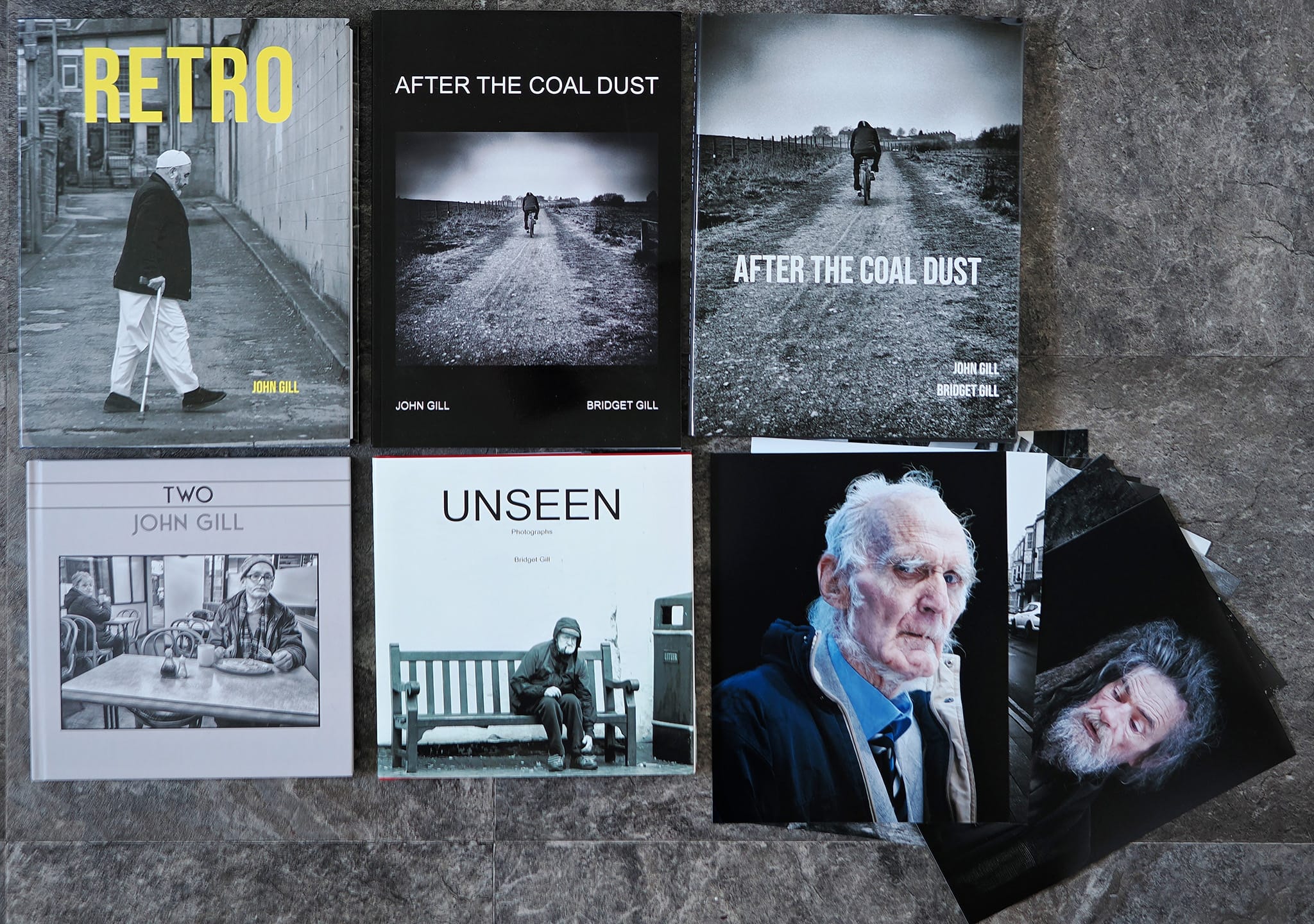 Christmas Book orders 7 A collection of photo books and prints titled "Retro," "After the Coal Dust," "Two," and "Unseen" by John Gill, displayed on a stone surface.