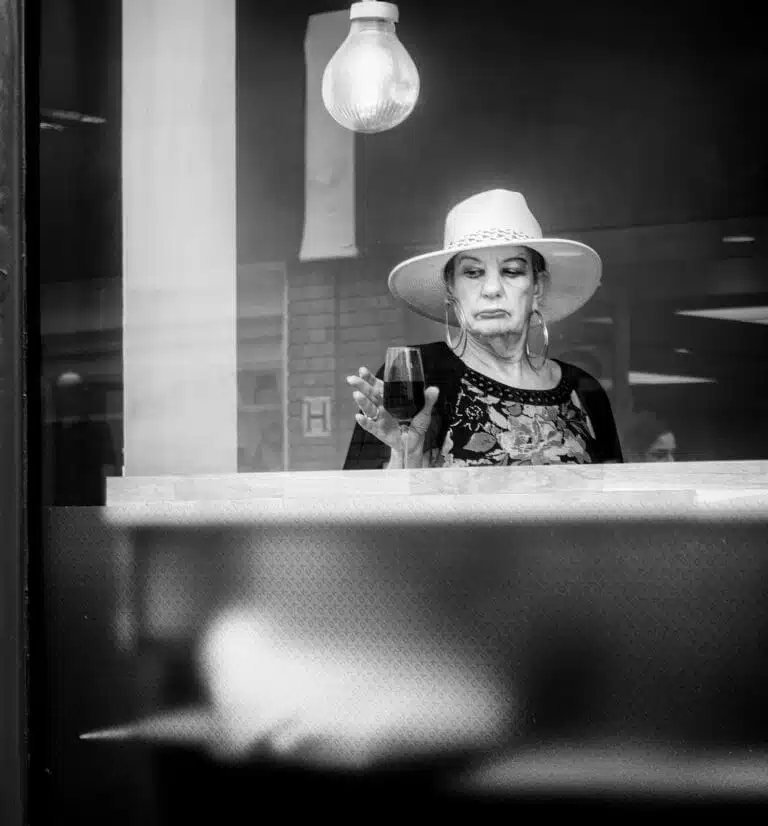 Woman in a hat stands behind a glass window, holding a glass, with a light bulb above her. Black and white image. Woman in a hat stands behind a glass window, holding a glass, with a light bulb above her. Black and white image.