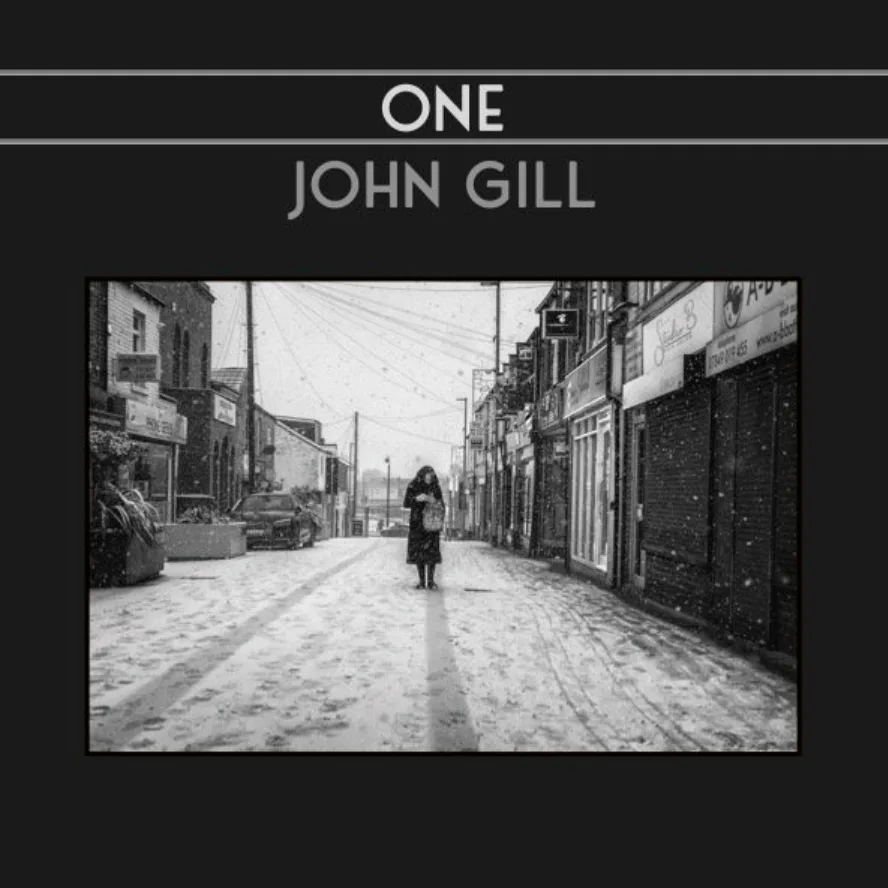 Black and white photo of a person walking alone down a snow-covered street lined with shops; text above reads "ONE JOHN GILL.